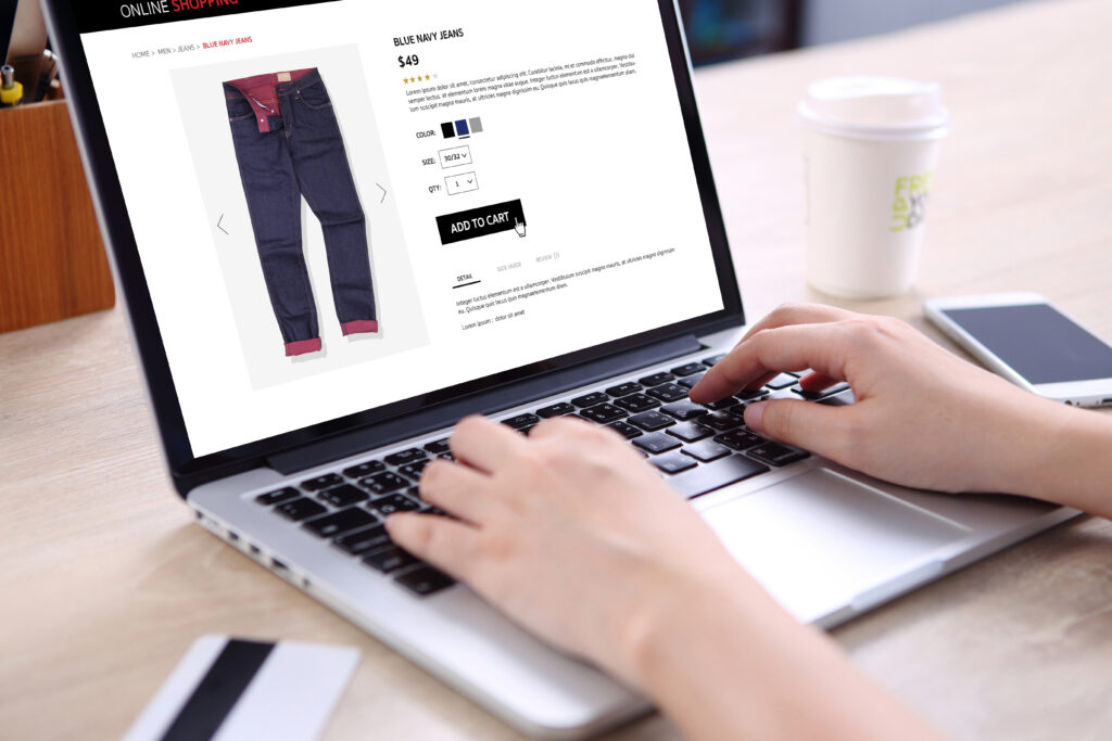 People buying blue navy jeans on ecommerce website with smart phone, credit card and coffee on wooden desk